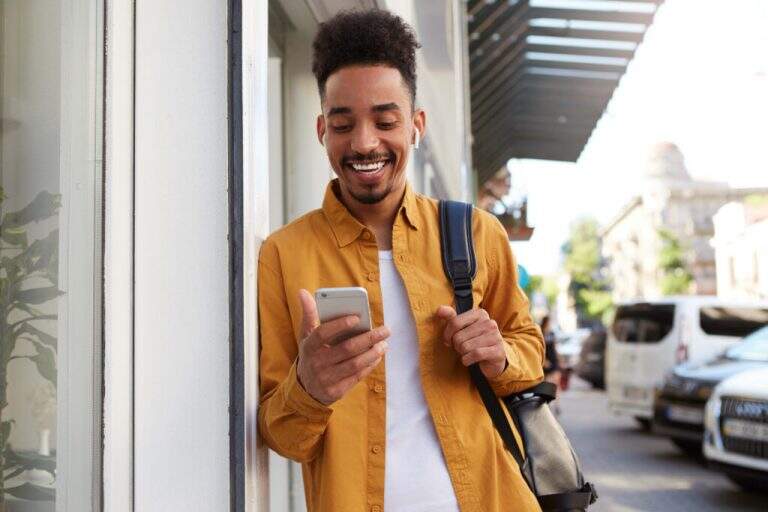 young cheerful african american guy yellow shirt walking down street holds telephone got message with funny video looks joyful broadly smiling x